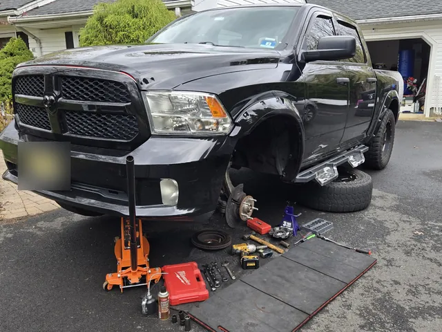A Ram 1500 up on stands, wheel off, tools laid out on mats