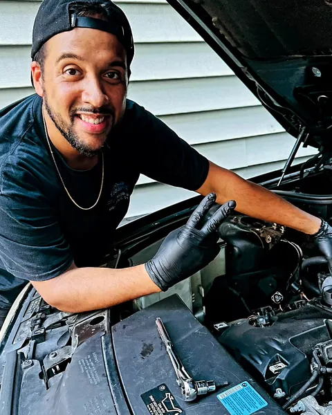 Steven Lopez, smiling, working under the hood of a BMW